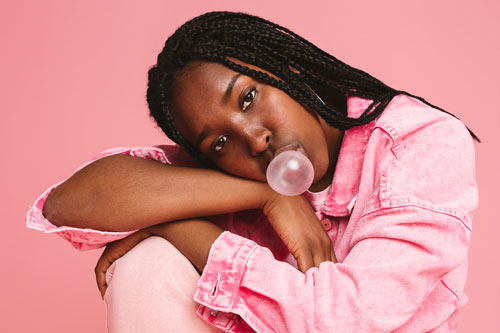 portrait of girl wearing pink jumpsuit in studio blowing bubble gum
