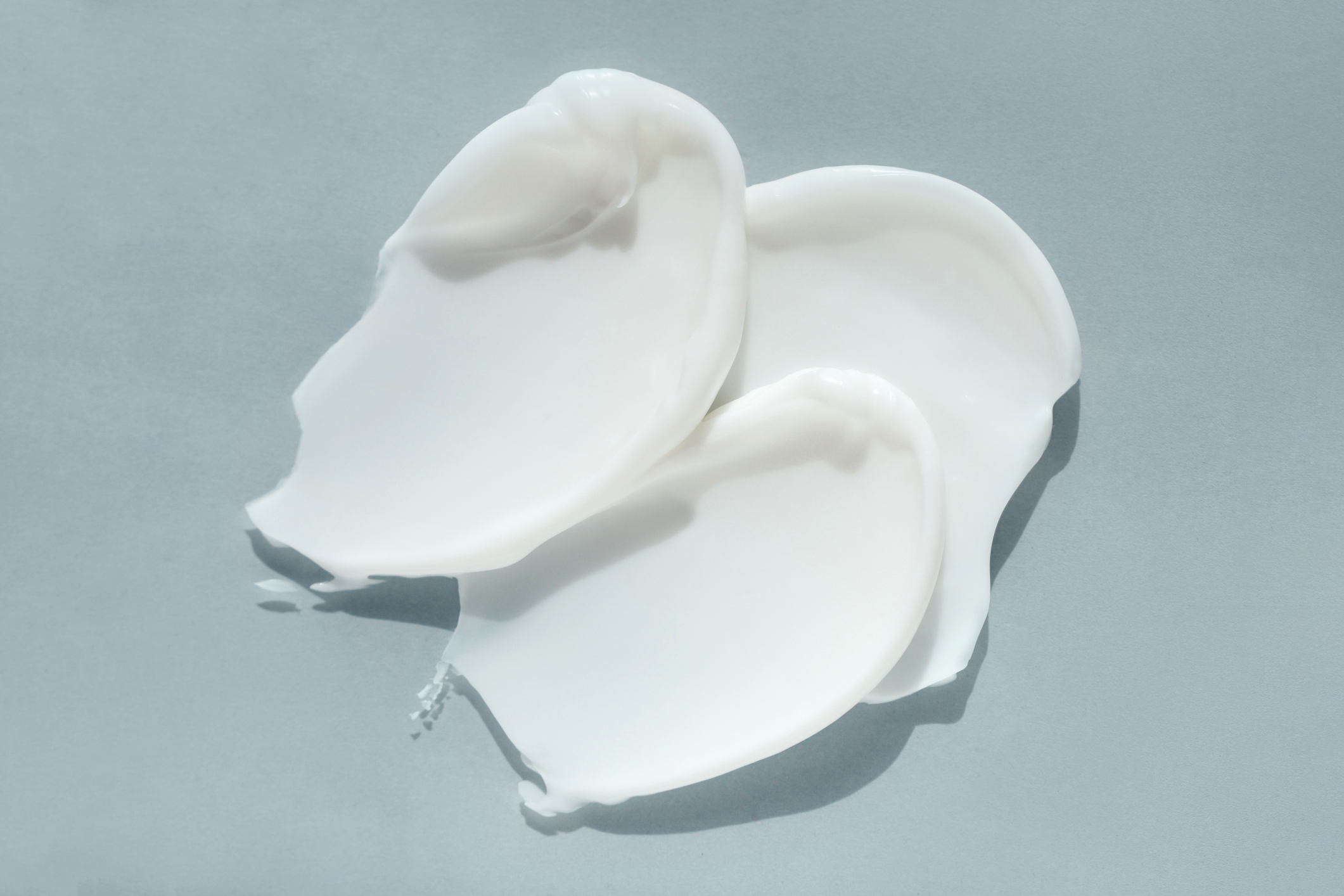 Smears of white yogurt or cream on light blue background. Flat lay style and close-up