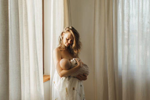 Portrait of mom and breastfeeding baby by window