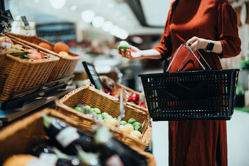 Cropped shot of a woman carrying a shopping basket, grocery shopping for fresh organic fruits and vegetables in supermarket