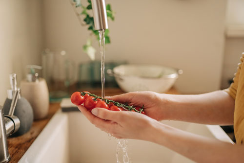 a woman washes spinach and tomatoes in the kitchen