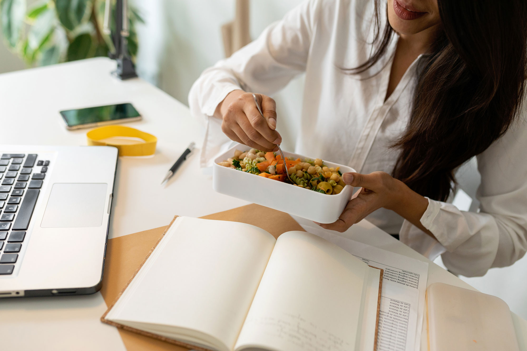 woman eating salad at her desk with laptop and notebook
