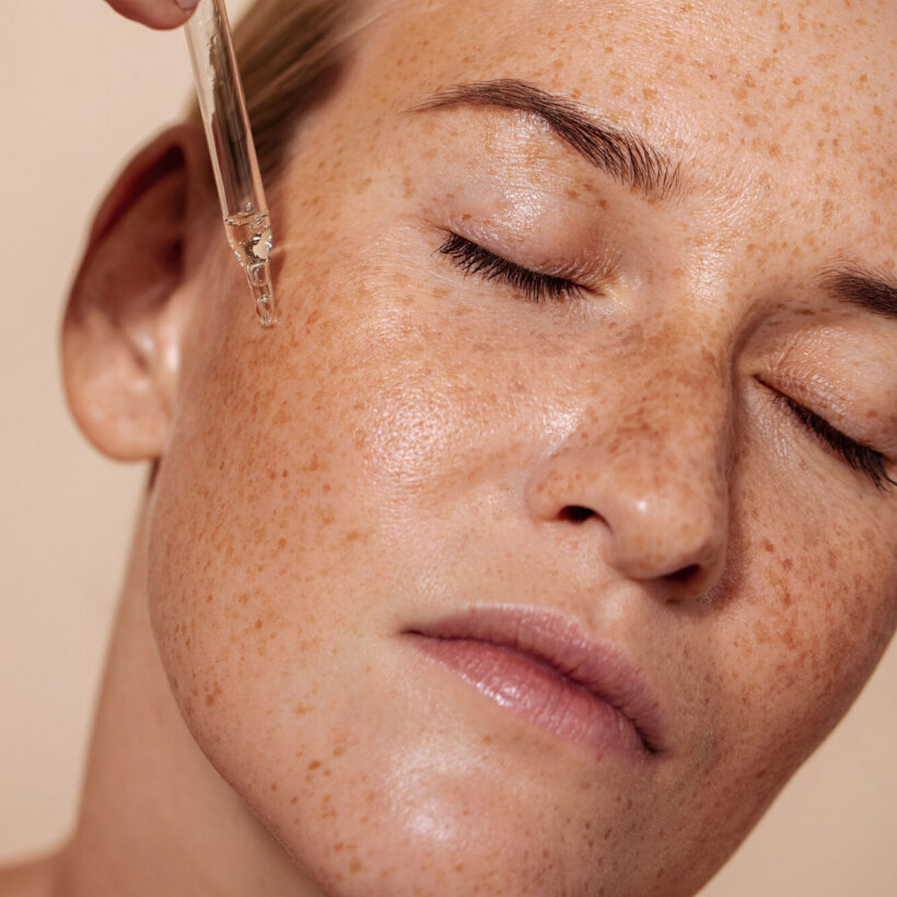 close up of woman with freckles applying serum