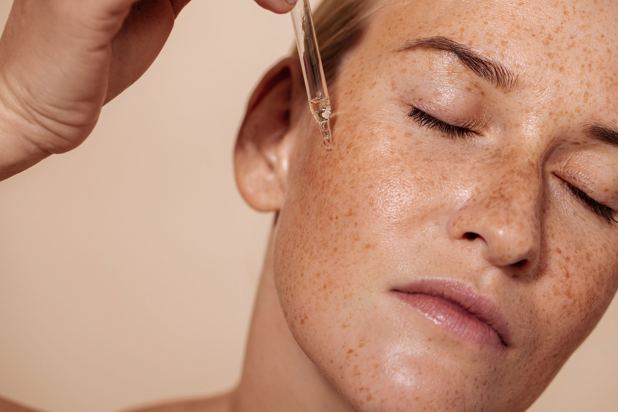 close up of woman with freckles applying serum
