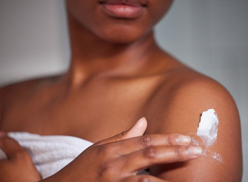 Shot of a woman applying lotion to her body