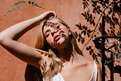 woman against wall with leaves shadow on face during sunny day