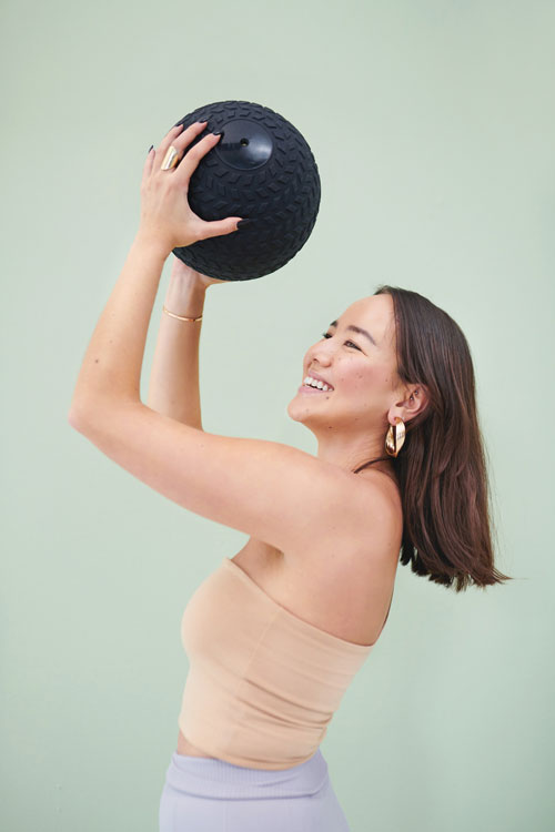 Cropped studio shot of a young woman posing with an exercise ball against a green background