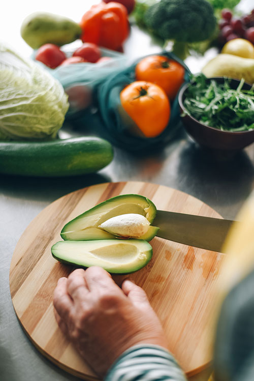 hand cutting avocado with Fresh vegetables on table