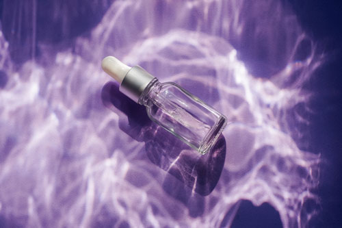 glass face serum bottle on purple background