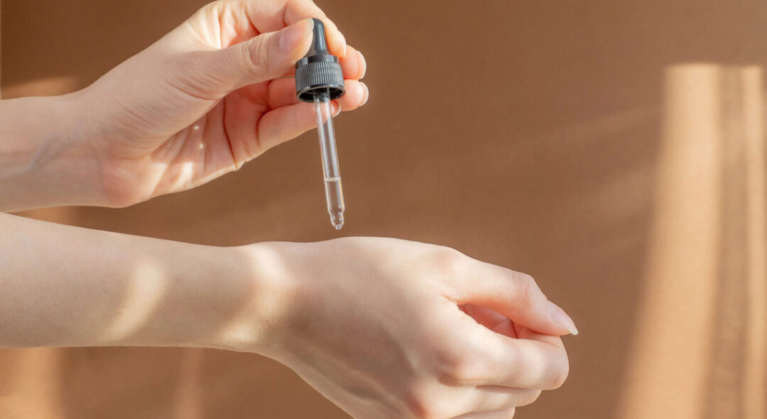 Pipette, with cosmetic serum, in women's hands on light brown background, in rays of sunlight