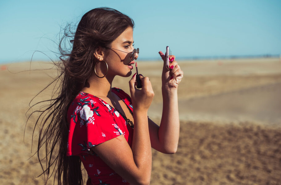 woman applying lip gloss on the beach