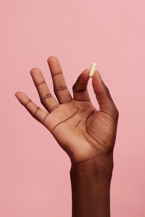 hand holding supplement pill on pink background