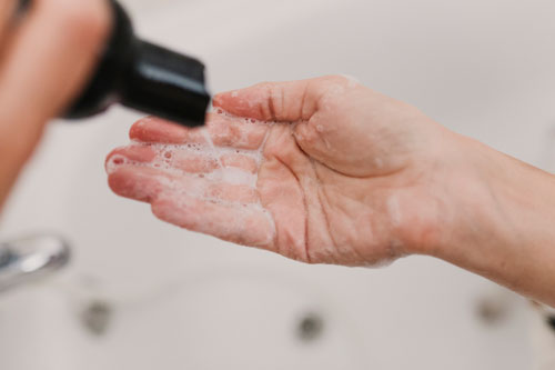 Cropped Hands Of Woman Removing cleanser From Bottle In Bathroom