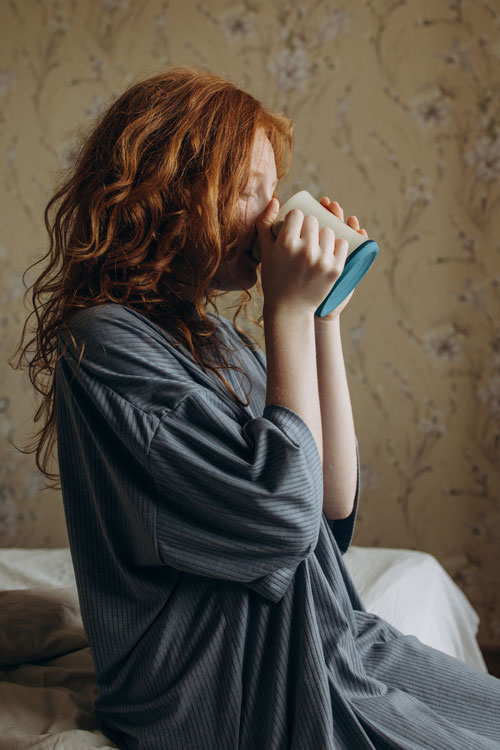 sick woman holding mug sitting on the bed