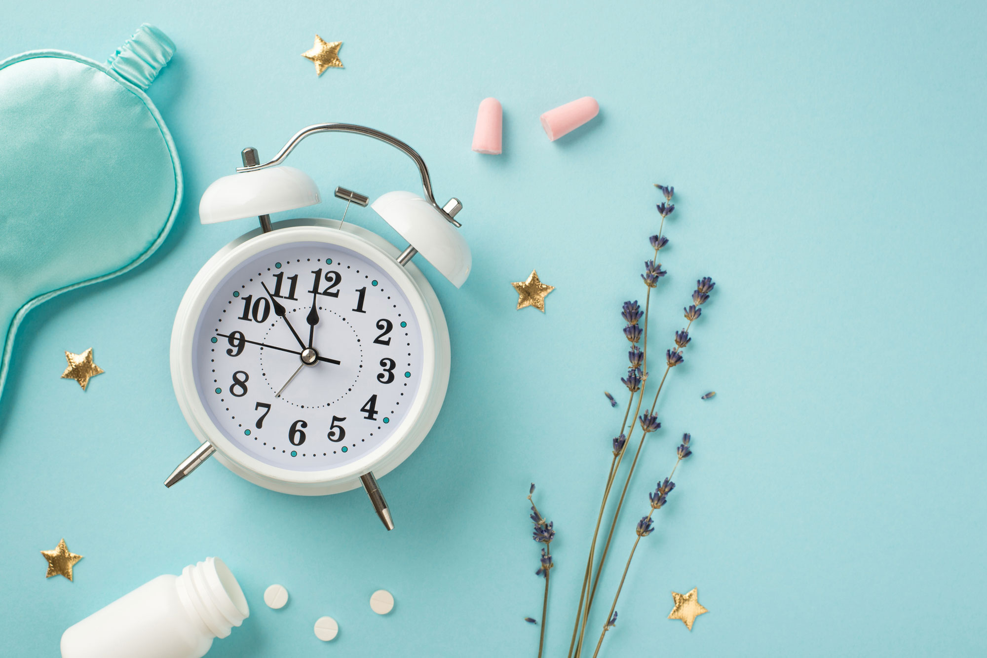 Top view photo of white alarm clock lavender blue satin sleeping mask pink earplugs open bottle with pills and golden stars on isolated pastel blue background