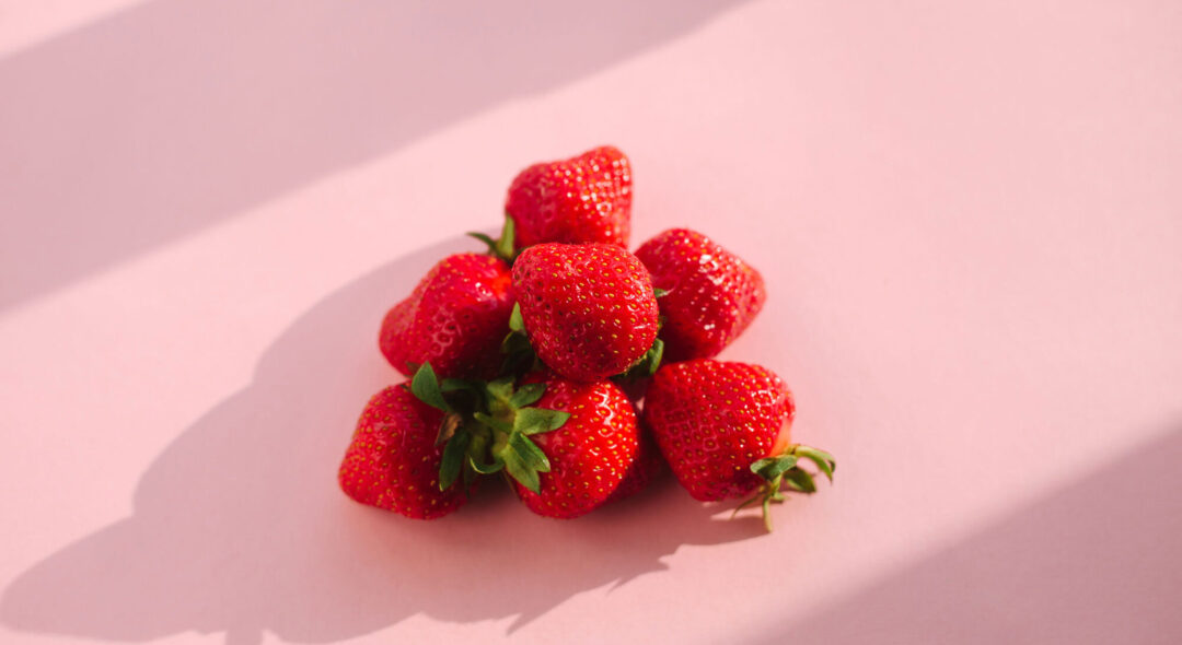 Red ripe strawberry fruits over pink background, bright sunlight
