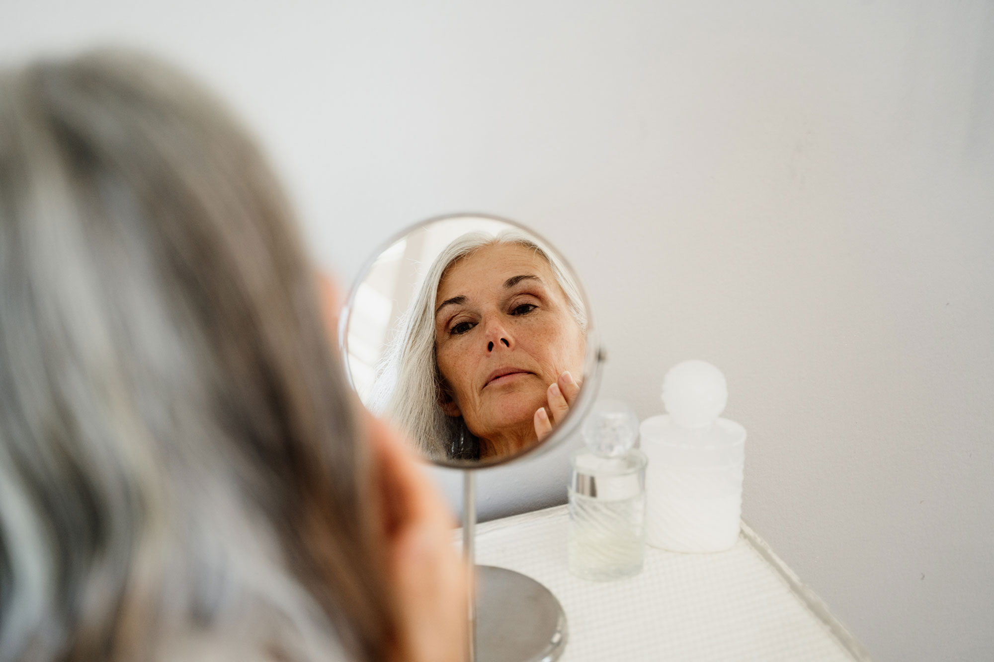 woman applying face cream in front of mirror