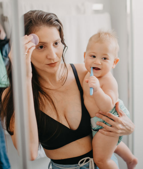 Mother getting ready in mirror while holding baby in the bathroom