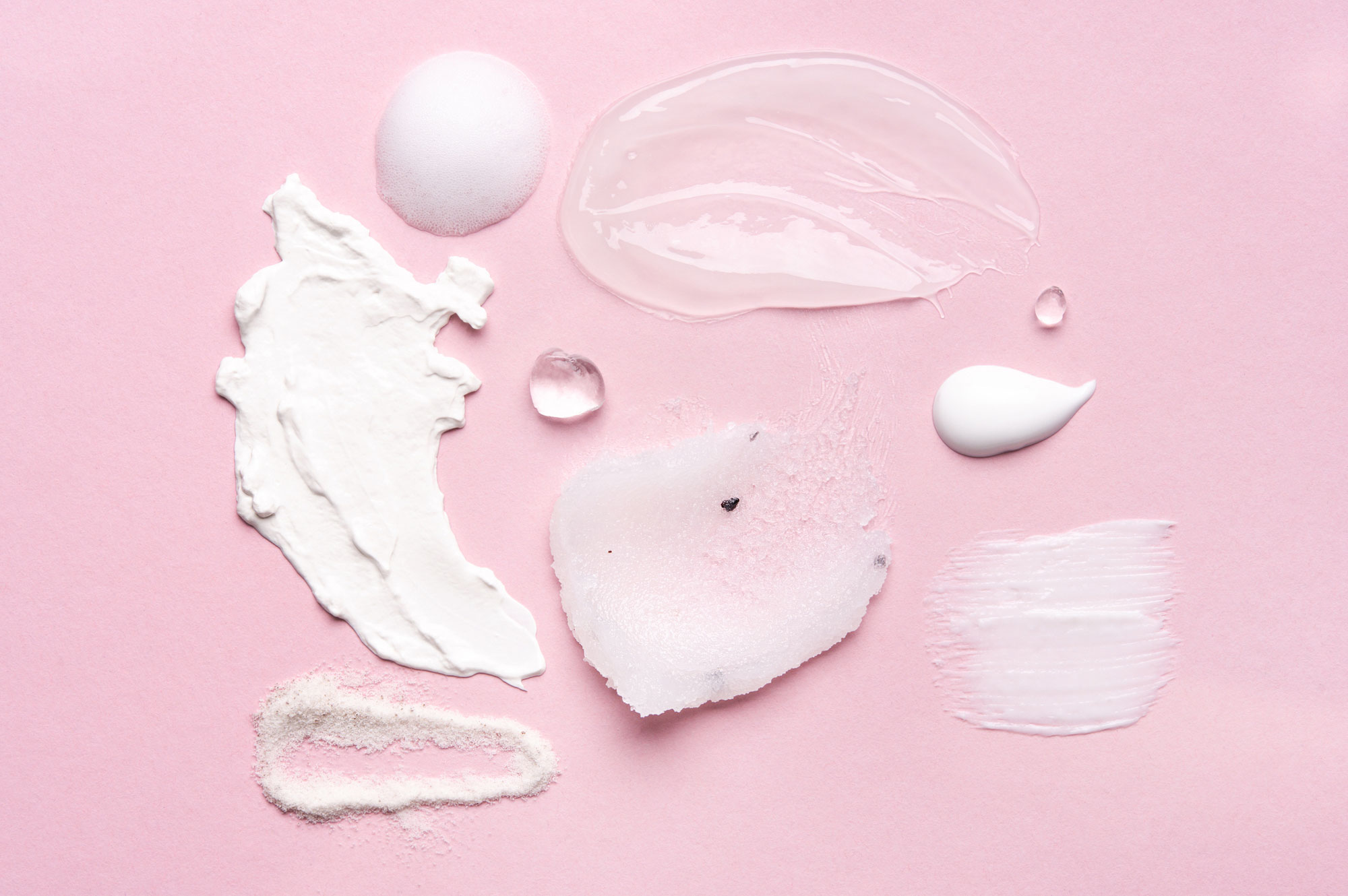 Set of cosmetic smears applied on pink background. Cleansing foam, lotions, scrubs, gels and moisturizing creams