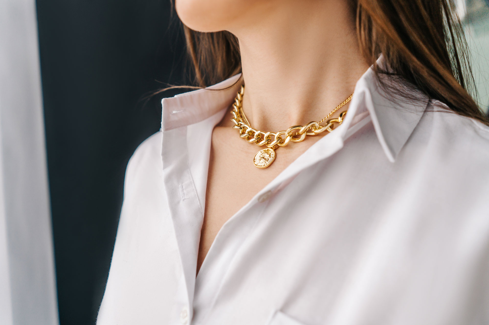 Close up of woman in a white shirt with gold chain necklaces.