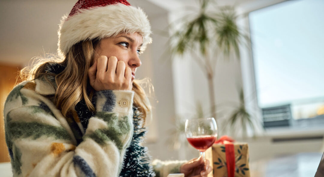 woman wearing a Santa hat drinking wine and thinking while spending time alone at home