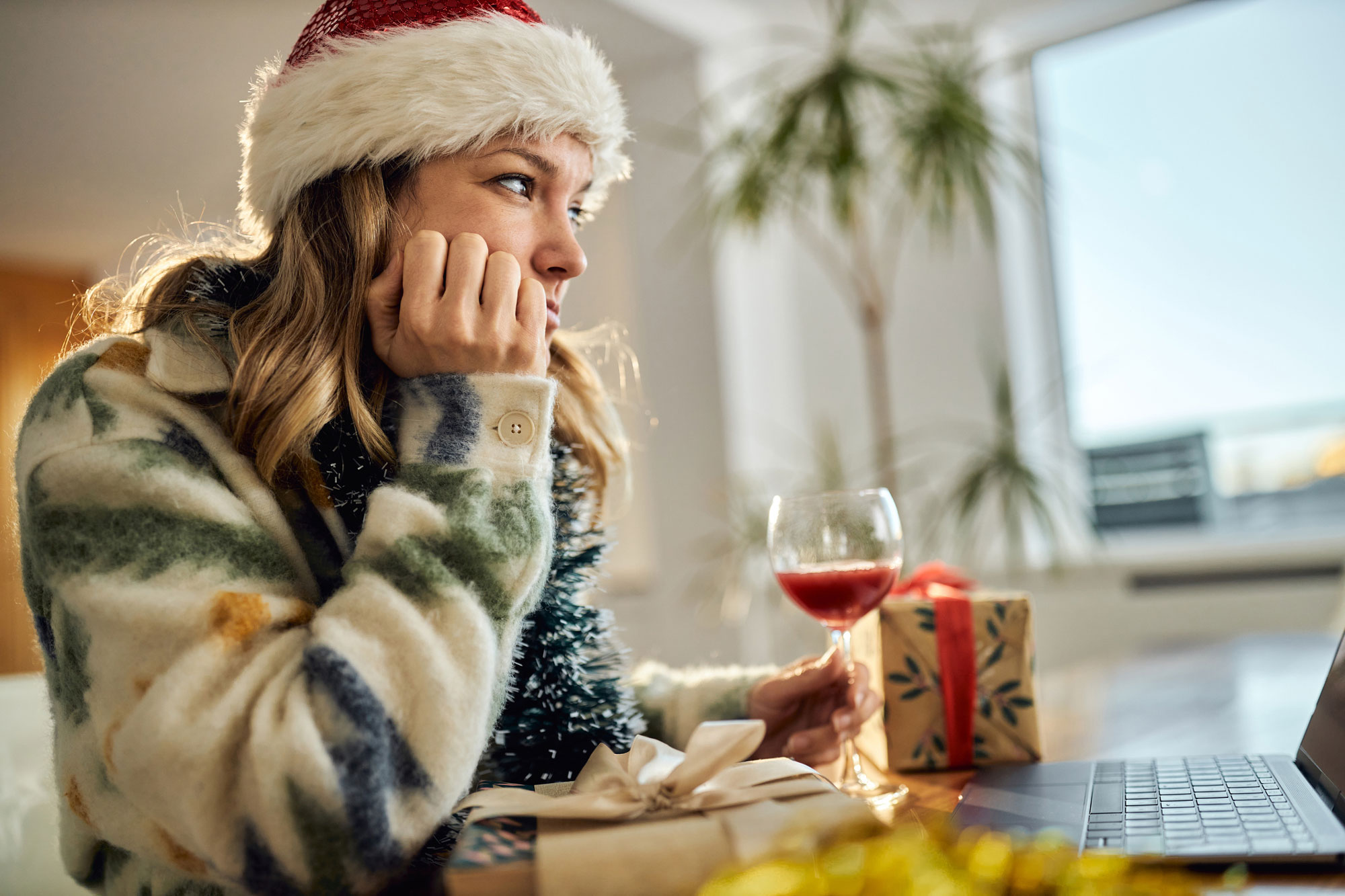 woman wearing a Santa hat drinking wine and thinking while spending time alone at home
