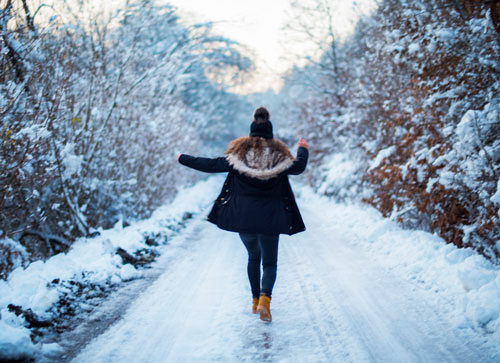 Rear View Of Happy Woman Walking On Snow Covered Road During Winter