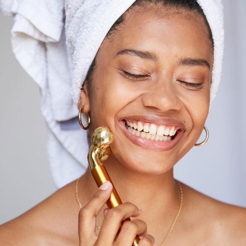 woman with head towel applying beauty tool on face