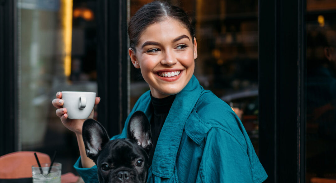 woman with her french bulldog, sitting in front of the restaurant, holding espresso cup and waiting for someone.
