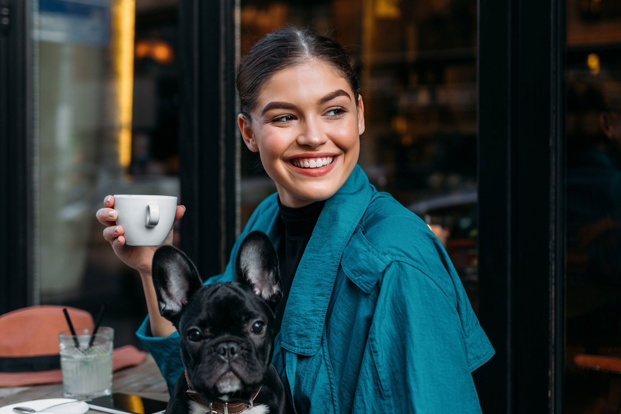 woman with her french bulldog, sitting in front of the restaurant, holding espresso cup and waiting for someone.