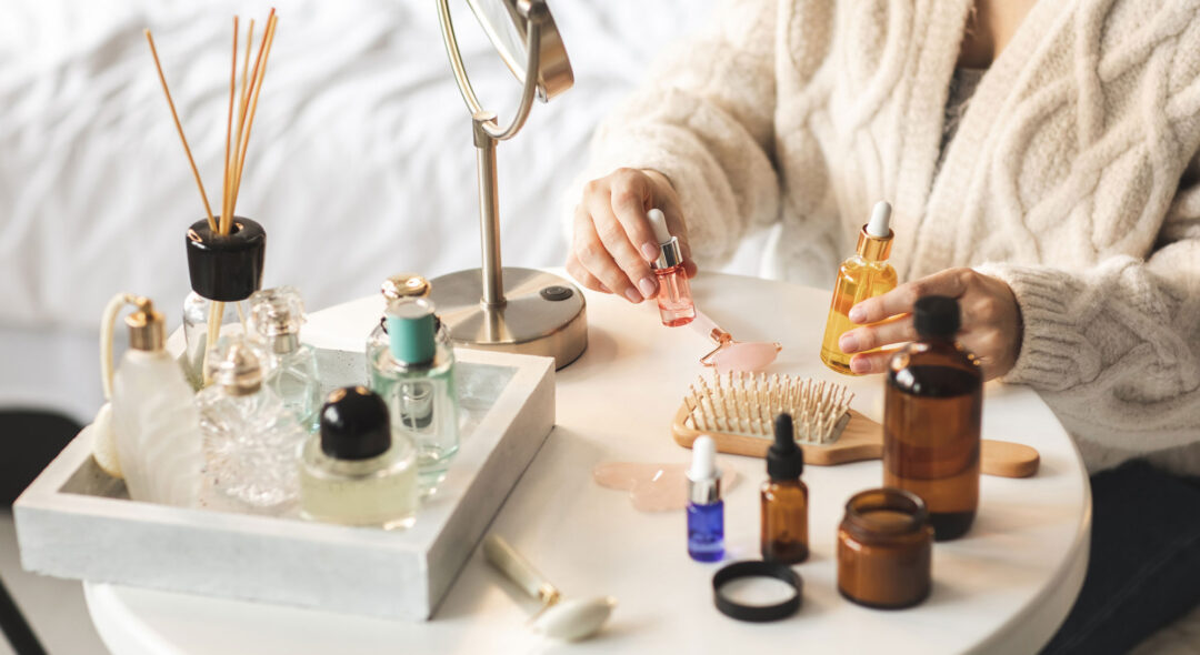 Beauty products laid out on a small white round table, woman's hands holding bottles with serum