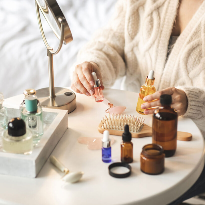 Beauty products laid out on a small white round table, woman's hands holding bottles with serum