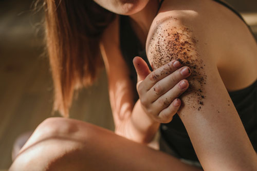 Woman applying coffee scrub on body