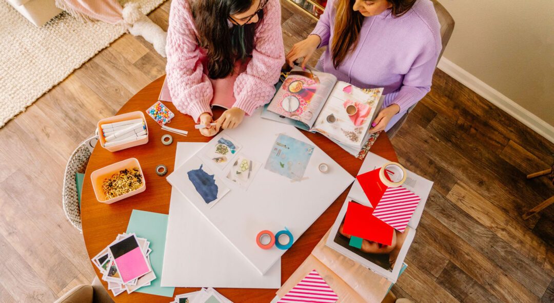Upper view mother and daughter cutting magazines and making a dream board out of photographs, magazines at a round table