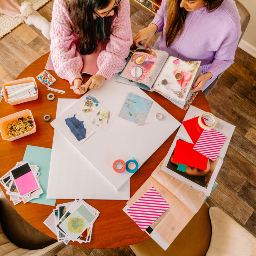 Upper view mother and daughter cutting magazines and making a dream board out of photographs, magazines at a round table