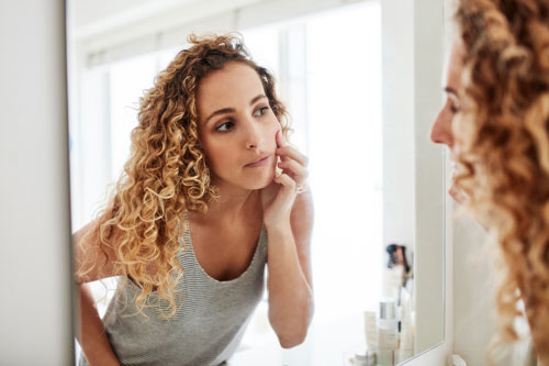 woman inspecting her face in the bathroom mirror
