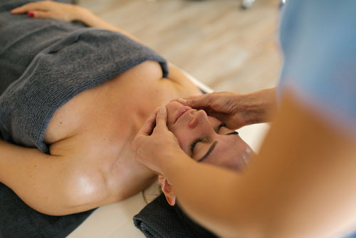 masseuse doing face massage at spa