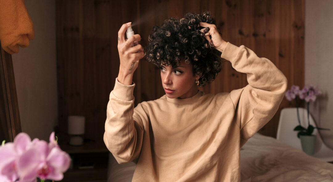 Woman with curly hair spraying hair product